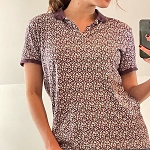 Lila-blommig pike - En lila och vit piké med blommor. Står storlek L men skulle mer säga s/m. Otroligt söt och i bra skick, knappt använd💜