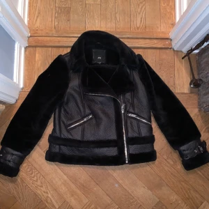 River Island Bikerjacka  - En svart bikerjacka från river island i konstgjort läder med snygga detaljer. Fodrad inuti vilket gör den perfekta jackan nu i vinter, både snygg och varm. Säljer då den inte kommer till användning i storlek S. Ursprungspris 1200 kr. Hör av er vid frågor:) 