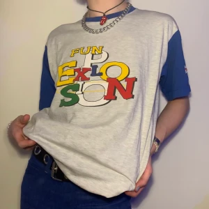 Vintage retro Reebok graphic tee t-shirt grå svart gul blå röd grön - Vintage grå Reebok graphic tee med färgglatt tryck som säger ”Fun Explotion” med den coolaste fonten i rött, blått, grönt, gult och svart samt blåa ärmar och krage 🧵 Min favoritdetalj med hela tröjan är den broderade Reebok loggan på vänster arm men även det kaotiska trycket på brösten vilket ger plagget så mycket karaktär! Den breda färgpaletten ger dig möjlighet att matcha den med så mycket! Du kan stylea den med ett par vintage bootcut jeans för en retro look men även ett par vanliga raka jeans för en mer vardaglig outfit! Matcha den även med accessoarer som komplimenterar färgerna i trycket för the cherry on top!
