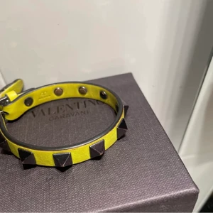 Valentino armband - Limited edition ”Nyon” gult Valentino armband, man ser att det är använd på bandet vid spännet annars bra skick. Box medföljer med påse och extra nitar!!