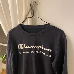 Marinblå/svart champion sweatshirt med vit text, sista bilden visar skicket på märket. 
