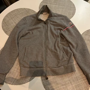 Moncler cardigan storlek M - Grå Moncler cardigan med dragkedja storlek M, passar S också. Grymt bra fit och passar till allt! Sparsamt använt och är 9/10 skick! Fri leverans inom Helsingborg annars står köparen för frakten!