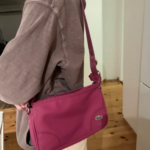 Lacoste väska - Annorlunda och cool väska! Har köpt second hand för ett tag sen men den kommer inte till användning. Bra ficka inuti och man kan välja själv om man ska axelbandet långt eller kort. Frakt tillkommer på 66kr:)