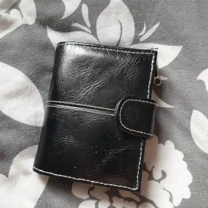 En fin svart plånbok i konstläder med vita sömmar! Finns månda fack, och ett rymligt myntfack med en silvrig dragkedja som man stänger och öppnar med ☺️ 