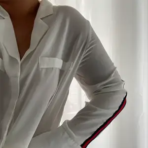 En vit snygg skjorta med snygga röda detaljer på båda ärmarna! Tyget är tunt så lite genomskinlig, dock meningen att de ska vara så! Köpt i stor storlek för att få till den där oversized looken på skjortan