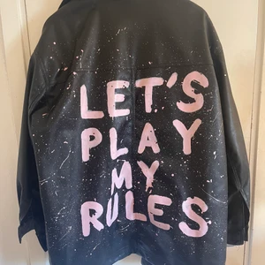 Skinnjacka - Skinnjacka från HM med egen skriven text på ryggen. Färgen sitter bra och har själv inte märkt några större släpp mm. Jackan är använd några få gånger men är i väldigt bra skick. Strl L, 200kr + frakt kostnad. Vid pris sänkning kom med bud då jag kan tänka mig att sänka lite vid snabb affär. 