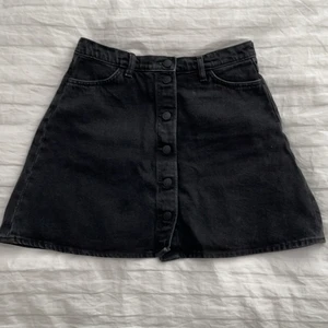 Jeanskjol strl 40 - Svart/grå jeanskjol från Monki i strl 40, den är använd ca 2 gånger alltså som ny. Den har fram och bakfickor och fina, svarta knappar längs framsidan. Köparen står för frakt och retuneras ej🖤