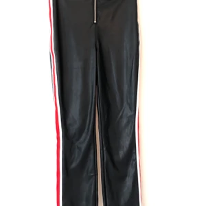 Svarta (faux) läderbyxor  - Säljer mina svarta (faux) läderbyxor med vita och röda stripes på sidorna och liten slits nertill. Storlek 38a men skulle säga att de passar en 36a/S-XS mer. Från Nakd.