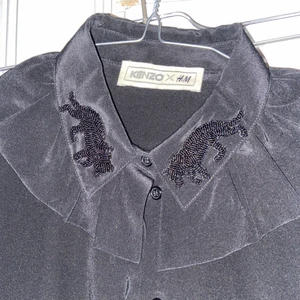 Silkesblus från HMxKENZO, oanvänd - Skjorta jag aldrig fått användning för. Svart aningen genomskinligt, skönt tyg av 100% silke. Helt oanvänd, ny skick. Storlek 36. Broderade tigrar på kragen och räfflade detaljer vid handlederna och kragen. Skriv vid frågor om exakta mått! 