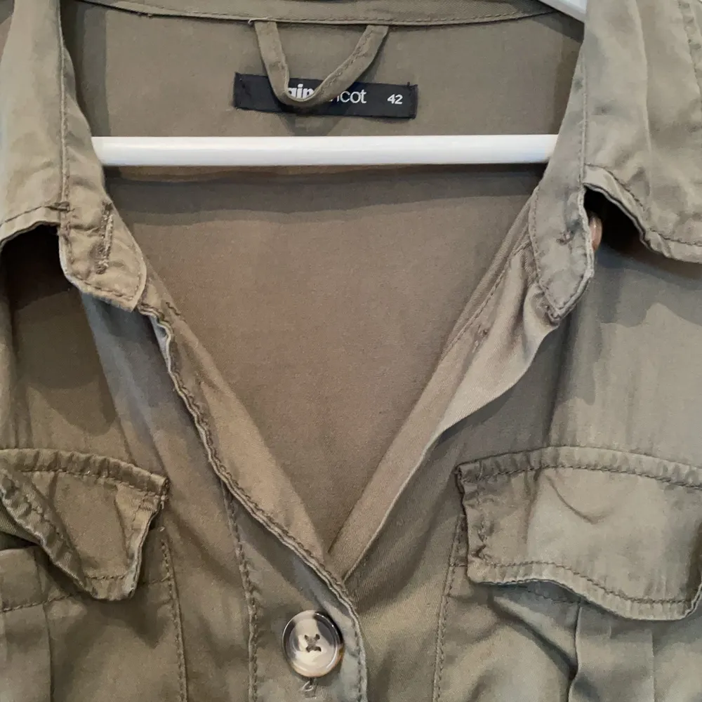 Snygg grön tunn jacka med knappar och fickor från Gina Tricot i storlek 42 (XL). Fint skick. Snöre i midjan som går att dra i.. Jackor.