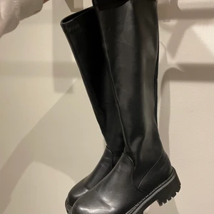 Svarta höga stövlar i skinn - Höga svarta stövlar i skinnimitation. De är storlek 40 men väldigt små i storlek så passar en 38/39. Aldrig använda, säljer enbart för att de är för små för mig. 