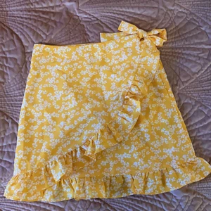 Kjol - Gul, blommig omlottkjol. I storlek S. Dragkedja finns på sidan och en knytning. Säljer den för att den inte kommit till användning och att den var lite kort. Skulle även passa XS. (Du betalar priset+frakt)