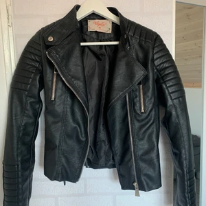 Chiquelle Moto Jacket Black - Snygg Mc-inspirerad jacka i läderimitation med quiltade detaljer på axlar och i ärmslut. Två fickor med dragkedja framtill. Reglerbara bälten på sidorna. Knappt använd, nypris 699kr