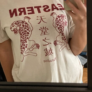 T-shirt  - Säljer denna beige/vita t-shirt med coolt rött tryck på. Den är i storlek XS men den är mer som en S. Den har en liten fläck men det märks inte. Tror det går bort i tvätten :)