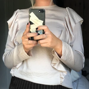 Topp med volanger - Festlig topp. Sparsamt använd så bra skick. Lite off white och glansig i färgen. Knäppningen till knappen bak i nacken har gått av men lätt att knäppa med min lilla säkerhetsnål (skickar med!) 🔥