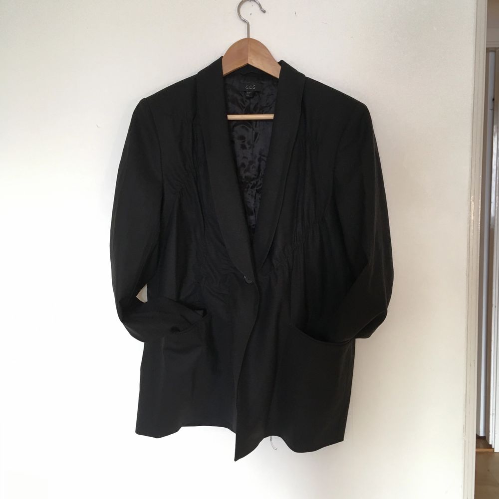 En assymetriskt veckad svart kavaj i tunn ull från Cos, så kallad sommarull som fungerar bra och andas när det är varnt. Storlek 38, oversize modell med fint fall i tyget. Jag har fler bilder på passformen som jag kan skicka! Superfina detaljer och jättefin kvalitet, den här förtjänar att bäras!. Jackor.