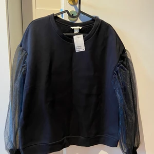 HM Sweatshirt med armarna i tyll - Cool sweatshirt från HM med armarna i tyll. Tyll liknar spets med sin seethrough effekt och ger en alternativt/mer elegant touch till den annars minimalistiska collegetröjan. Tröjan är ny med etikett. Storlek L (men passar även en M om man har vill ha en mer relaxed look). Aldrig använt pga att jag köpte två olika storlekar. 
