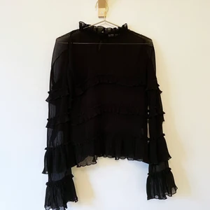 Svart blus med volanger - Svart blus från NAKD med volanger. Ganska transparent med räfflade partier mellan volangerna.
