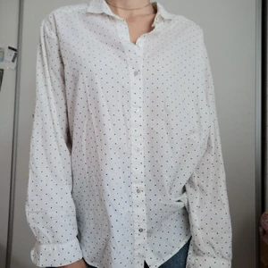 Vit skjorta med små svarta hjärtan - Skjorta från hm med pyttesmå svarta hjärtan, storlek 38. Så snygg till blå jeans eller en fin kjol! Användbar året runt som kofta på sommaren eller under stickad tröja på vintern och hösten. Sitter oversize på mig som brukar ha storlek 36.