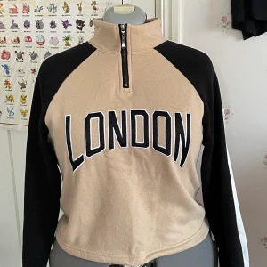 Cropped sweatshirt med zipper turtleneck - Cropped sweatshirt i beige, svart och vit. Med London brodera detalj, turtleneck med zipper och justerbar midja. Storlek L men kan justeras till mindre, sydocka är i storlek L. Köpt på New yorker. Kan skickas eller möttas upp, köparen står för frakten. Betalning sker via swish och meddela mig gärna om frågor och detaljer. <3