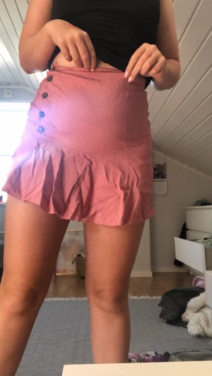 Rosa kjol i storlek xs från zara - En rosa kjol från zara med volanger och insydda underbyxor och bruna knappar. Väldigt fin färg och passform. Använt kanske en gång.