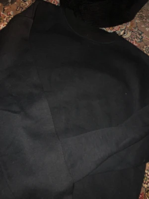 Svart hoodie från Boohoo - En enkel och stilren svart hoodie från Boohoo i storlek XL. Tillverkad i mjukt material med klassisk passform och ribbade muddar vid ärmslut och nederkant. Perfekt för en avslappnad look.