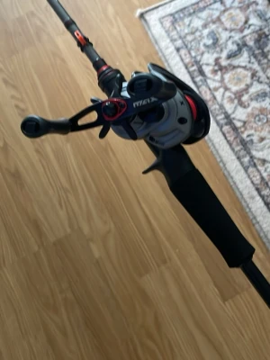 Svart fiskespö med rulle - Säljer ett svart fiskespö med tillhörande rulle. Spöet har detaljer i rött och grått samt ett greppvänligt handtag i svart material. Perfekt för dig som gillar fiske och vill ha ett smidigt spö med modern design.