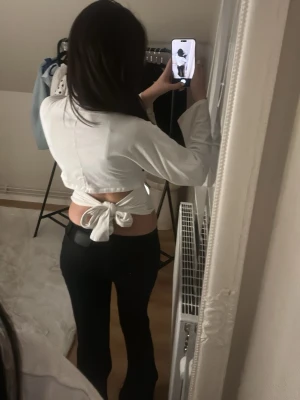 Vit croppad topp med knyt i ryggen - Säljer en vit croppad topp med långa vida ärmar och snygg knytning i ryggen. Toppen är i ett tunt, stretchigt material och har en enkel, stilren design som passar perfekt till jeans eller kjol.