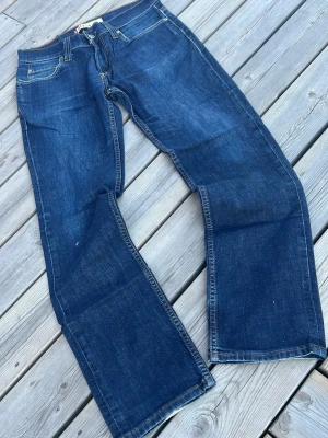 Levi's 517 Slim blå jeans - Säljer ett par klassiska Levi's 517 Slim jeans i mörkblå denim. Jeansen har fem fickor, raka ben och snygga kontrastsömmar. Perfekta för dig som gillar tidlös stil och vill ha ett par jeans som funkar till det mesta. Materialet är slitstark bomullsdenim.