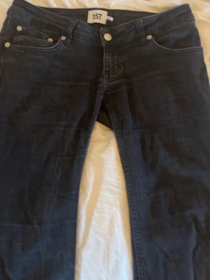 Svarta bootcut jeans - Säljer ett par svarta bootcut jeans med klassisk femficksmodell och normal midja. Jeansen har en lätt utsvängd passform nedtill och är tillverkade i ett stretchigt denimtyg som sitter snyggt på kroppen. Perfekta för dig som gillar en tidlös look.De är från lager 157. Och har blivit lite blekta i tvätten och har små sträck på sig.