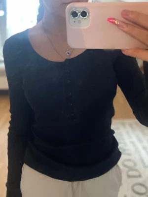 Svart ribbad långärmad topp - Snygg svart långärmad ribbad topp med knappar framtill. Vet inte vart ifrån den är eller storlek men passar s-m🖤