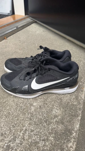 Svarta Nike Vapor Pro tennisskor - Säljer ett par svarta Nike Vapor Pro tennisskor med vit sula. Skorna har snörning. Perfekta för gymmet, tennis eller löpning. Snygg och sportig design med låg profil. Finns ej att köpa längre, just denna modell!! Nypris 1300kr. Använda fåtal gånger