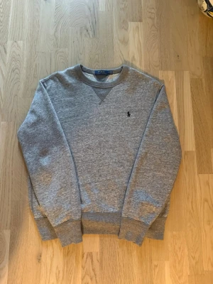 Grå sweatshirt från Polo Ralph Lauren - Säljer en grå polo ralph lauren tröja då den inte används längre, den är i bra skick. Den har lite mjukare och skönare material innuti. Hör av dig vid frågor eller funderingar!