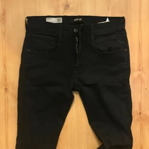 Svarta Replay jeans med smal passform - Säljer ett par svarta jeans från Replay med smal passform och klassisk femficksdesign. Jeansen har dragkedjegylf och Replay-logga på bakfickan samt patch bak i midjan. Perfekta för dig som gillar stilrena och tidlösa jeans.size 31/34
