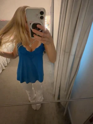 Blå linnetopp med spetsdetaljer - Snygg blå linnetopp med tunna axelband och spetsdetaljer längs urringningen. Toppen har en lös passform och är perfekt för varma dagar. Enkel att styla med både jeans och kjol.