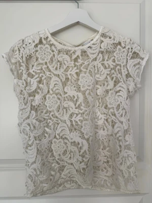Vit spetsblus från Gina Tricot - Säljer en superfin vit spetsblus från Gina Tricot i storlek 34. Blusen har korta ärmar och ett detaljerat blommigt spetsmönster som ger en romantisk vibe. Perfekt att styla med jeans eller kjol för en trendig look.💕