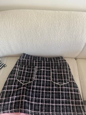 Sister Jane kjol (oanvänd) - Säljer en snygg kortkjol med rutigt mönster i svart, rosa och vitt. Kjolen har två framfickor med guldfärgade detaljer och är gjord i ett tjockare tyg som känns lite som tweed. Perfekt för dig som vill ha en trendig och chic look.