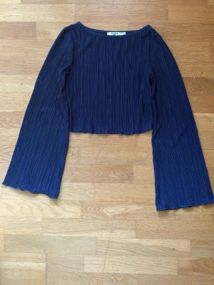 Mörkblå croppad topp från NA-KD - Trendig mörkblå croppad topp från NA-KD med långärmad design och ribbad struktur. Toppen har vida ärmar och en enkel rund halsringning. Perfekt för dig som vill ha en stilren men ändå unik look.