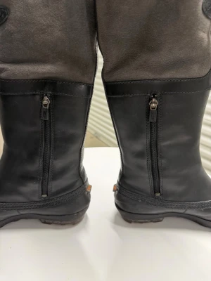 Svarta höga stövlar med snörning - Snygga höga stövlar i svart med detaljer i mörkgrått. Stövlarna har dragkedja bak och snörning upptill på sidan. Tillverkade i en kombination av läder och mocka, med robust sula som passar för höst och vinter.