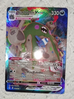 Pokémonkort Garbodor VMAX holo - Säljer ett Garbodor VMAX Pokémonkort med holografisk yta. Kortet har färgstark design med Garbodor i fokus och detaljer i grönt, lila, blått och rött. Det är ett samlarkort från Pokémon TCG och har en unik glansig finish.