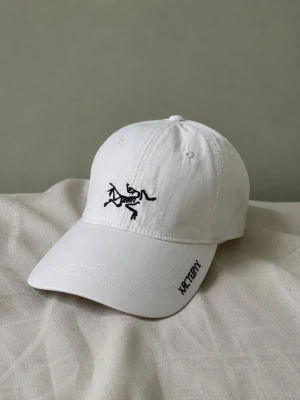keps Arc'teryx - Snygg vit keps från Arc'teryx med svart broderad logga framtill och text på skärmen. Klassisk böjd skärm och justerbar passform. Tillverkad i ett lätt och bekvämt material som passar perfekt till streetwear eller casual outfits.