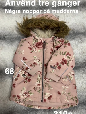 Rosa blommig vinterjacka med fuskpäls - Jättefin rosa vinterjacka med blommigt mönster och huva med fluffig fuskpäls. Jackan har dragkedja framtill, två fickor och reflexdetaljer på ärmarna. Perfekt för kyliga dagar och ger en gullig vibe.🌸 Använd tre gånger. Några noppor på muddarna som blev direkt. Storlek 68