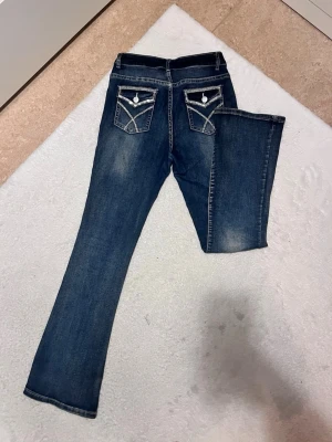 Mörkblå bootcut jeans med detaljer - Skitsnygga mörkblå bootcut jeans med kontrastsömmar. Bakfickorna har dekorativa lock och knappar som ger extra edge. Jeansen har en klassisk femficksmodell och är tillverkade i stretchigt denim för skön passform.
