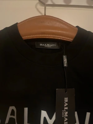 Svart Balmain Paris t-shirt - Snygg svart t-shirt från Balmain Paris med vit logga tryckt framtill. Klassisk rund halsringning och korta ärmar. Perfekt för dig som vill ha en stilren och trendig look med exklusiv känsla.