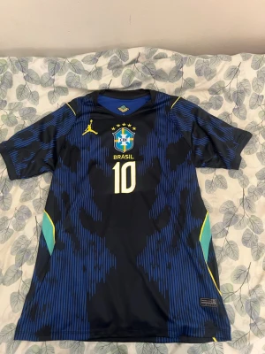 Neymar jr - Säljer en blå och svart Brasilien fotbollströja med nummer 10 och CBF-emblem på bröstet. Tröjan har gula detaljer, korta ärmar och ett sportigt mönster. Perfekt för dig som älskar fotboll och vill stötta Brasilien på match eller träning.