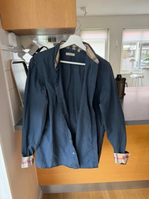Burberry skjorta  - Tja!  Säljer nu denna grymt snygga Burberry skjorta i populära mörkblåa färgen. Perfekt nu inför sommaren! Storlek L, men sitter mer eller mindre som en perfekt M. Bra skick på skjortan, väl omhändertagen. Självklart är skjortan äkta/autentisk Priset ej hugget i sten men snabba affärer prioriteras.  Allt gott