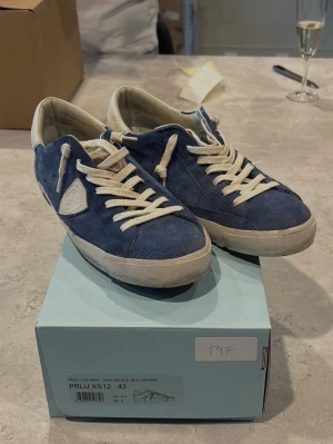Philippe model skor storlek 43 - Ett par sneakers från Philippe Model i blått. Skorna har vita skosnören och en vit sula. Skorna har en logotyp på sidan. 