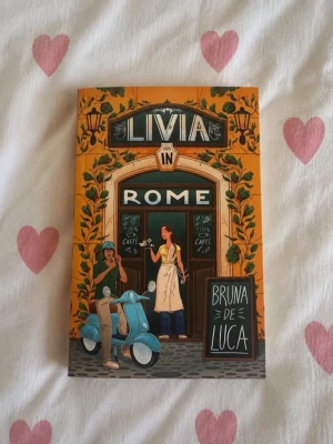 Livia in Rome – Bruna De Luca | Häftad | Nyskick - Livia in Rome av Bruna De Luca i nyskick. Läst en gång och mycket väl omhändertagen utan synliga veck, markeringar eller skador. En mysig feelgood-romance med italiensk sommarkänsla. Perfekt för dig som älskar romantik, Rom och semesterläsning. Skickas väl emballerad. ✨