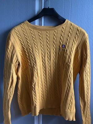 Gul kabelstickad tröja  Bondelid - Gul kabelstickad tröja från Bondelid. Klassisk modell med rund hals, ribbade muddar och broderat.