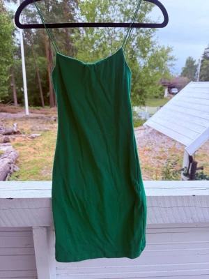 Grön kort klänning med tunna band - Säljer en grön, figurnära kort klänning med tunna axelband. Klänningen har en enkel och stilren design som ger en snygg siluett. Perfekt för dig som gillar minimalistisk stil och vill ha något bekvämt men ändå trendigt.